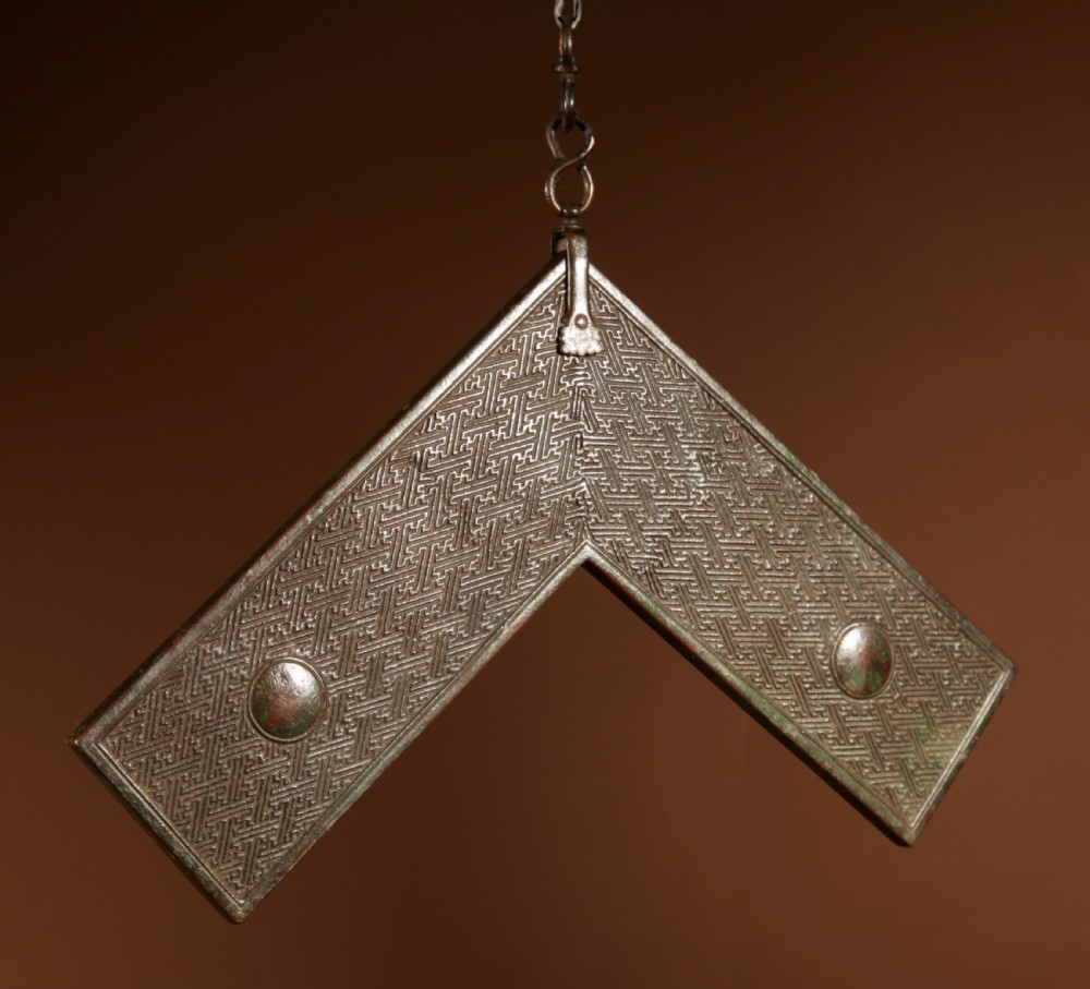 A chevron-shaped cast bronze musical chime featuring geometric relief patterns and a top suspension loop. View II