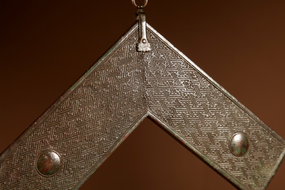 A chevron-shaped cast bronze musical chime featuring geometric relief patterns and a top suspension loop. View VI