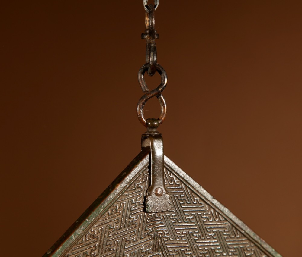 A chevron-shaped cast bronze musical chime featuring geometric relief patterns and a top suspension loop. View VII