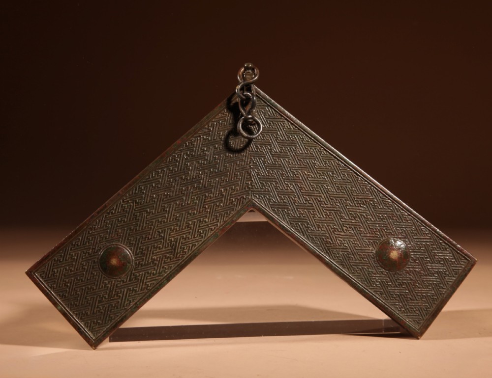 A chevron-shaped cast bronze musical chime featuring geometric relief patterns and a top suspension loop. View IX