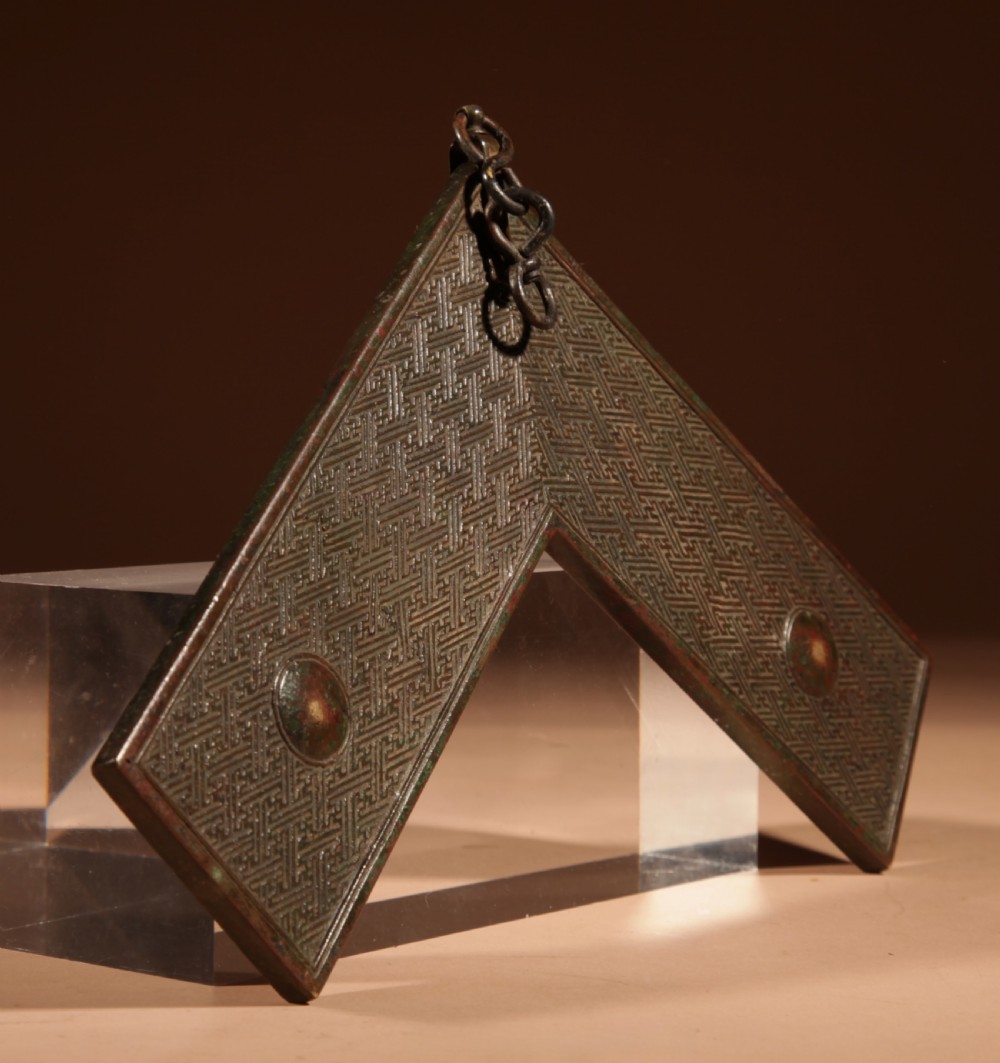 A chevron-shaped cast bronze musical chime featuring geometric relief patterns and a top suspension loop. View X