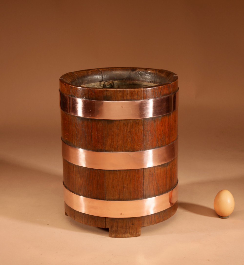 A cylindrical dark oak planter constructed with vertical timber staves, bound by three horizontal copper bands, and supported by small wooden feet.
