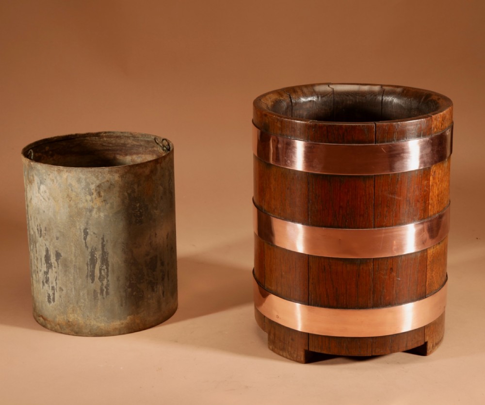 A cylindrical dark oak planter constructed with vertical timber staves, bound by three horizontal copper bands, and supported by small wooden feet. View III