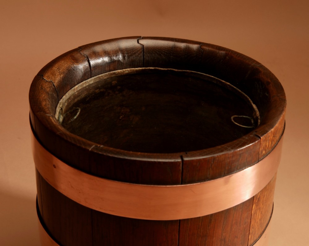 A cylindrical dark oak planter constructed with vertical timber staves, bound by three horizontal copper bands, and supported by small wooden feet. View IV