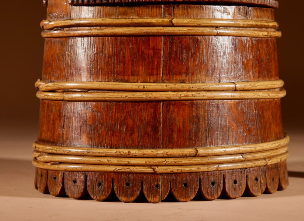 An oval oak butter tub featuring coopered staves, bound wood hoops, two raised side handles, a carved scalloped base, and a fitted lid with a turned central finial. View II
