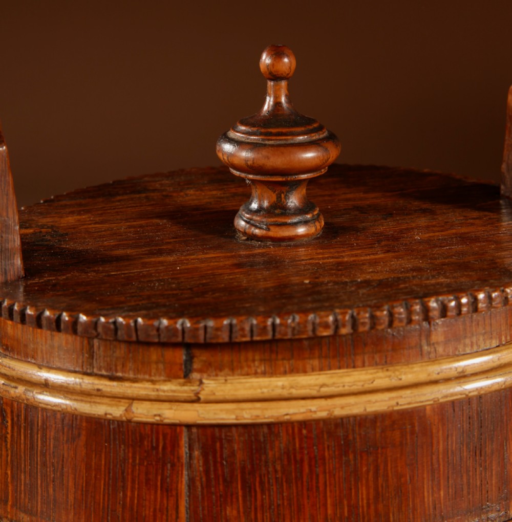 An oval oak butter tub featuring coopered staves, bound wood hoops, two raised side handles, a carved scalloped base, and a fitted lid with a turned central finial. View VIII