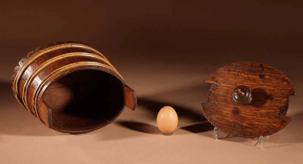 An oval oak butter tub featuring coopered staves, bound wood hoops, two raised side handles, a carved scalloped base, and a fitted lid with a turned central finial. View IX
