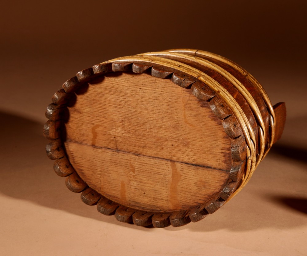 An oval oak butter tub featuring coopered staves, bound wood hoops, two raised side handles, a carved scalloped base, and a fitted lid with a turned central finial. View X
