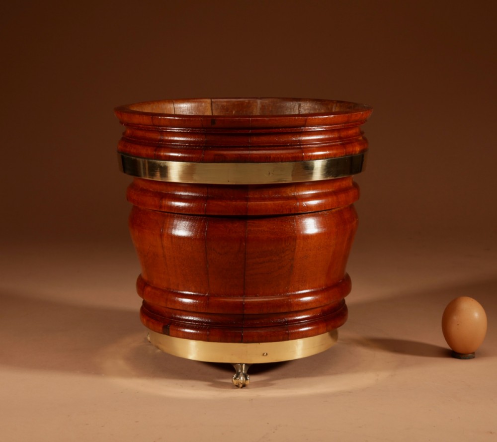 A coopered mahogany circular planter featuring polished brass banding and small brass feet.