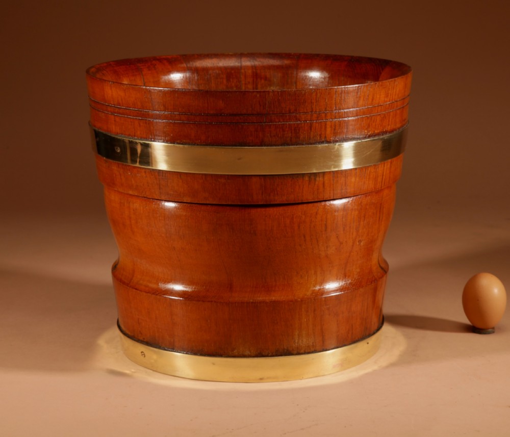 A turned teak planter featuring brass binding bands around the upper rim and base.