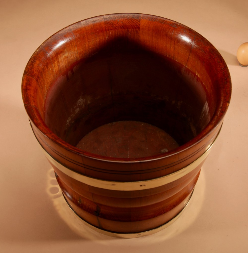A turned teak planter featuring brass binding bands around the upper rim and base. View V