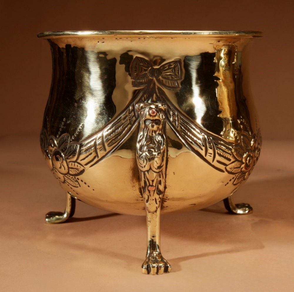 A pair of polished brass jardinieres featuring embossed floral swags and resting on tripod lion paw feet. View III