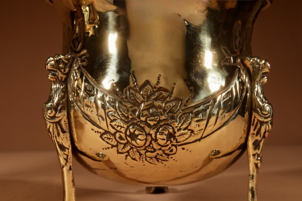 A pair of polished brass jardinieres featuring embossed floral swags and resting on tripod lion paw feet. View IV