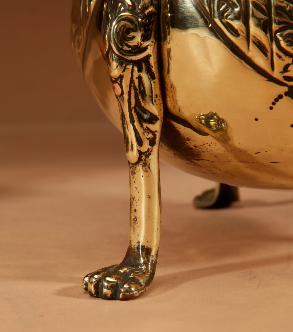 A pair of polished brass jardinieres featuring embossed floral swags and resting on tripod lion paw feet. View VI