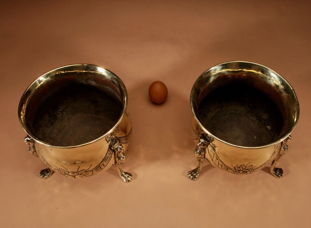 A pair of polished brass jardinieres featuring embossed floral swags and resting on tripod lion paw feet. View IX