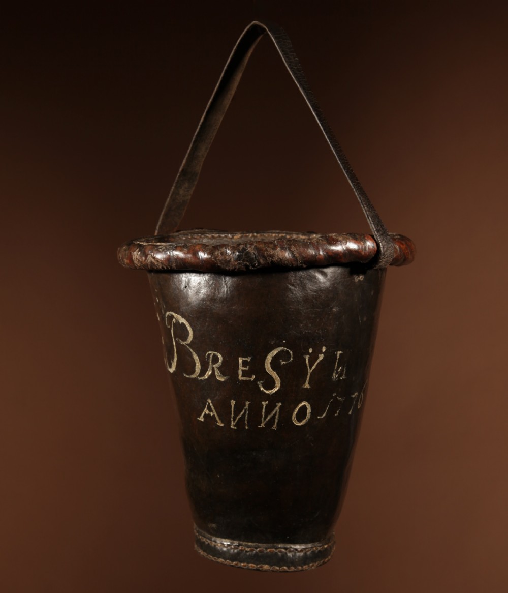 An 18th-century dark brown leather fire bucket featuring a tall stitched leather handle, a thick rolled rim, and hand-painted cream lettering reading BRESYL ANNO 1776.