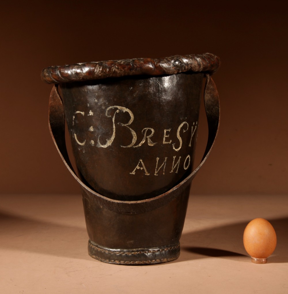 An 18th-century dark brown leather fire bucket featuring a tall stitched leather handle, a thick rolled rim, and hand-painted cream lettering reading BRESYL ANNO 1776. View II
