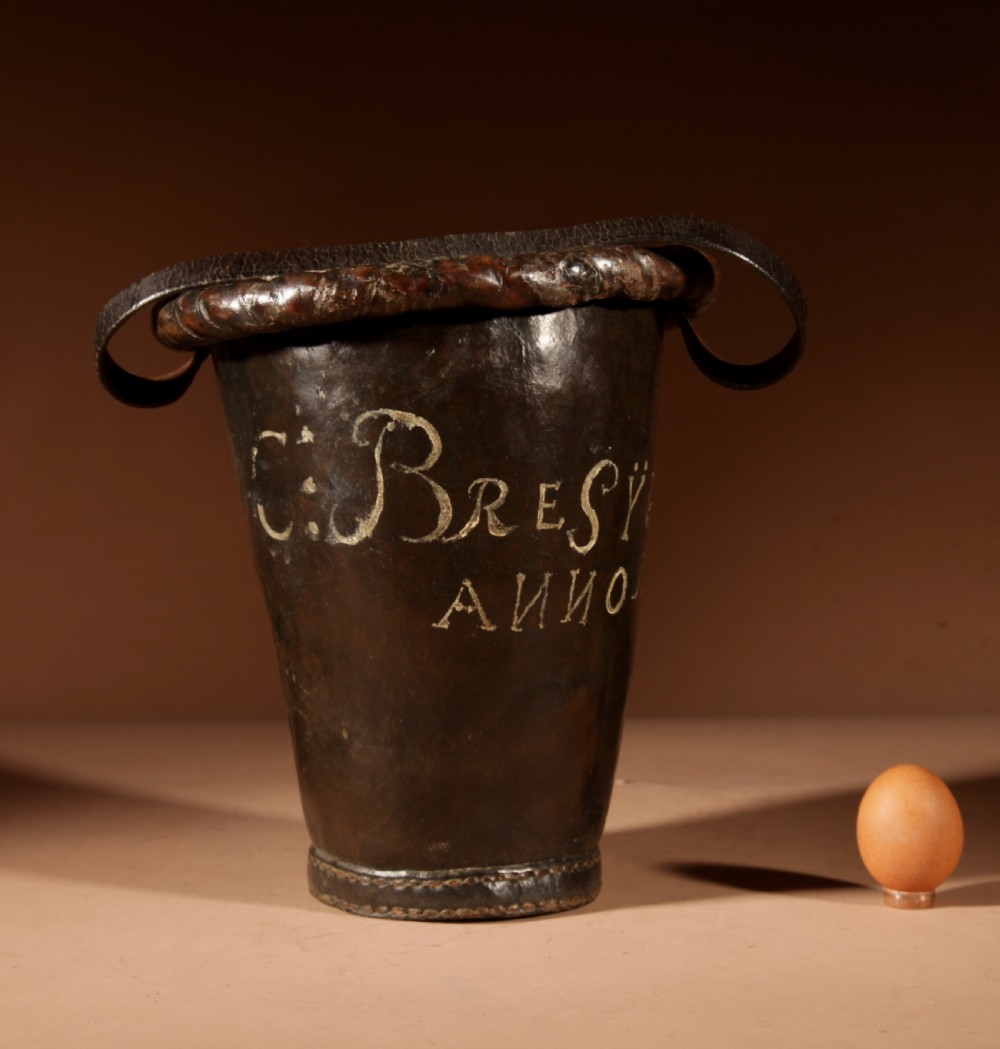 An 18th-century dark brown leather fire bucket featuring a tall stitched leather handle, a thick rolled rim, and hand-painted cream lettering reading BRESYL ANNO 1776. View III