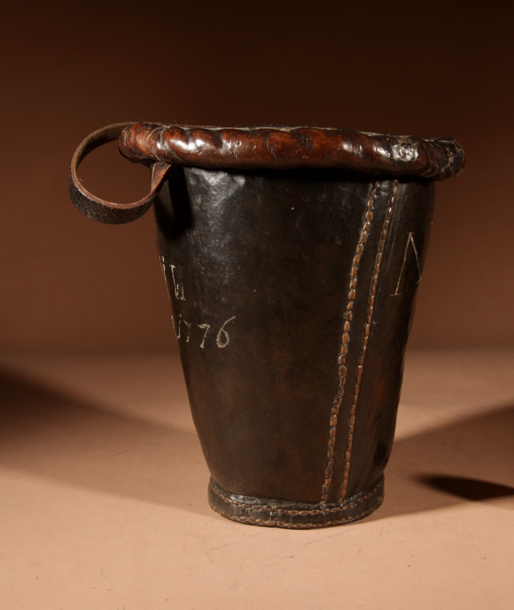 An 18th-century dark brown leather fire bucket featuring a tall stitched leather handle, a thick rolled rim, and hand-painted cream lettering reading BRESYL ANNO 1776. View VI