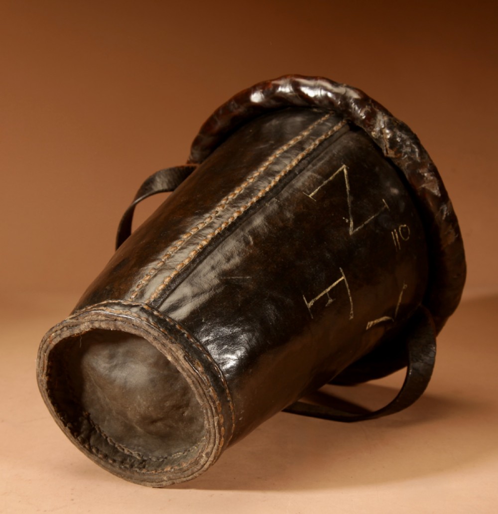 An 18th-century dark brown leather fire bucket featuring a tall stitched leather handle, a thick rolled rim, and hand-painted cream lettering reading BRESYL ANNO 1776. View X