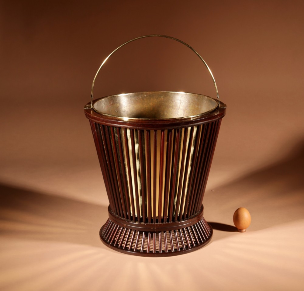 A 19th-century mahogany peat bucket constructed with open vertical spindles, a fitted brass interior liner, and a swinging brass handle.