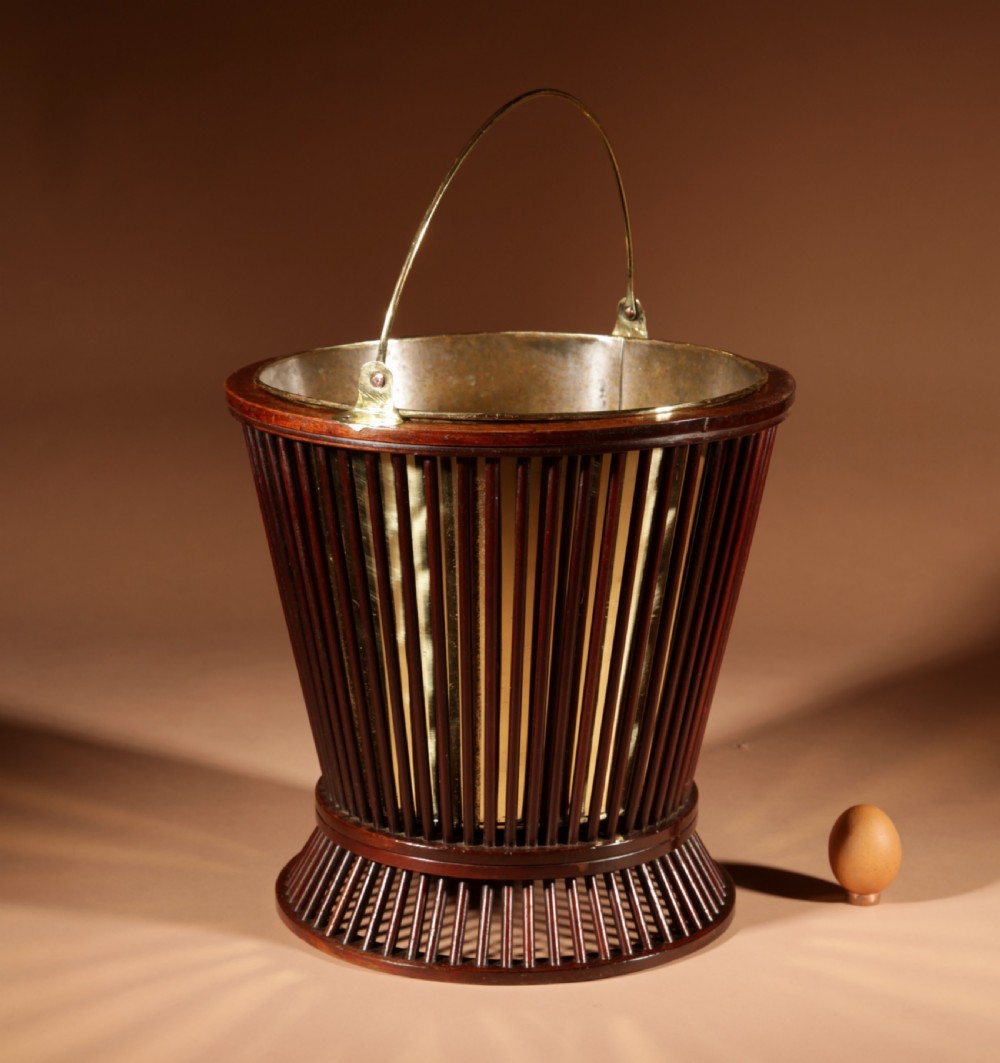 A 19th-century mahogany peat bucket constructed with open vertical spindles, a fitted brass interior liner, and a swinging brass handle. View II