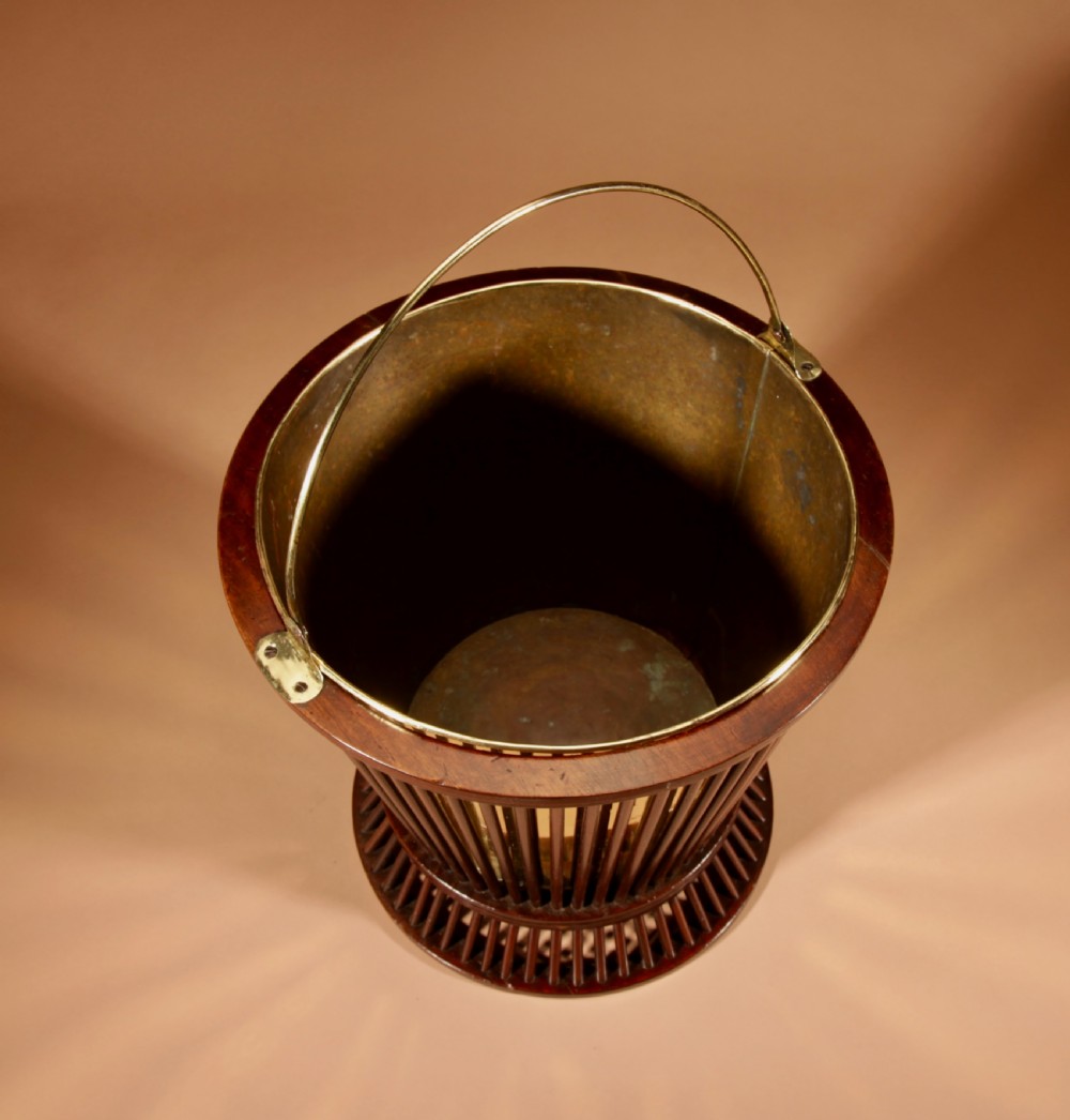 A 19th-century mahogany peat bucket constructed with open vertical spindles, a fitted brass interior liner, and a swinging brass handle. View IV