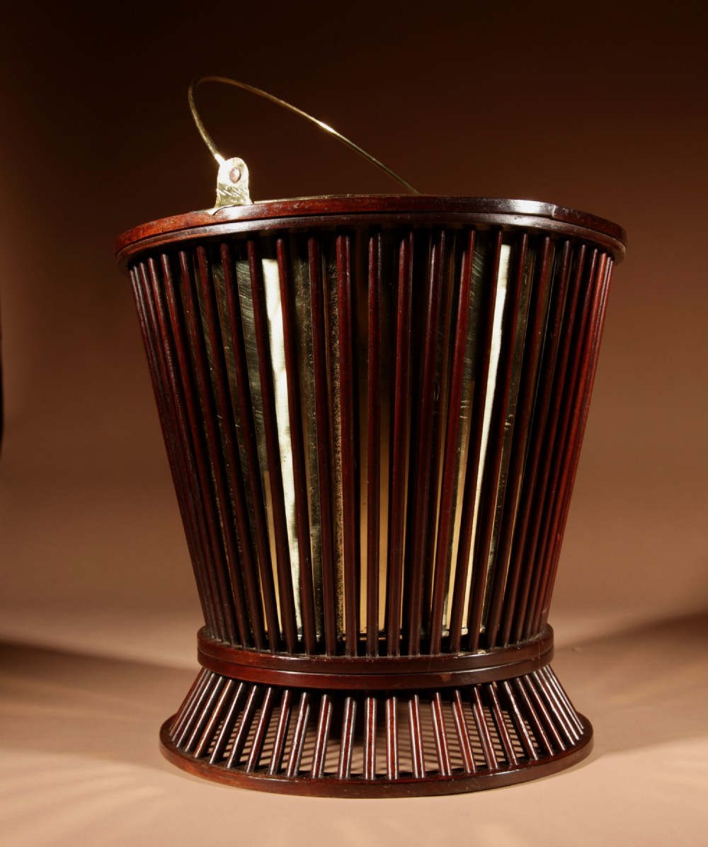 A 19th-century mahogany peat bucket constructed with open vertical spindles, a fitted brass interior liner, and a swinging brass handle. View V