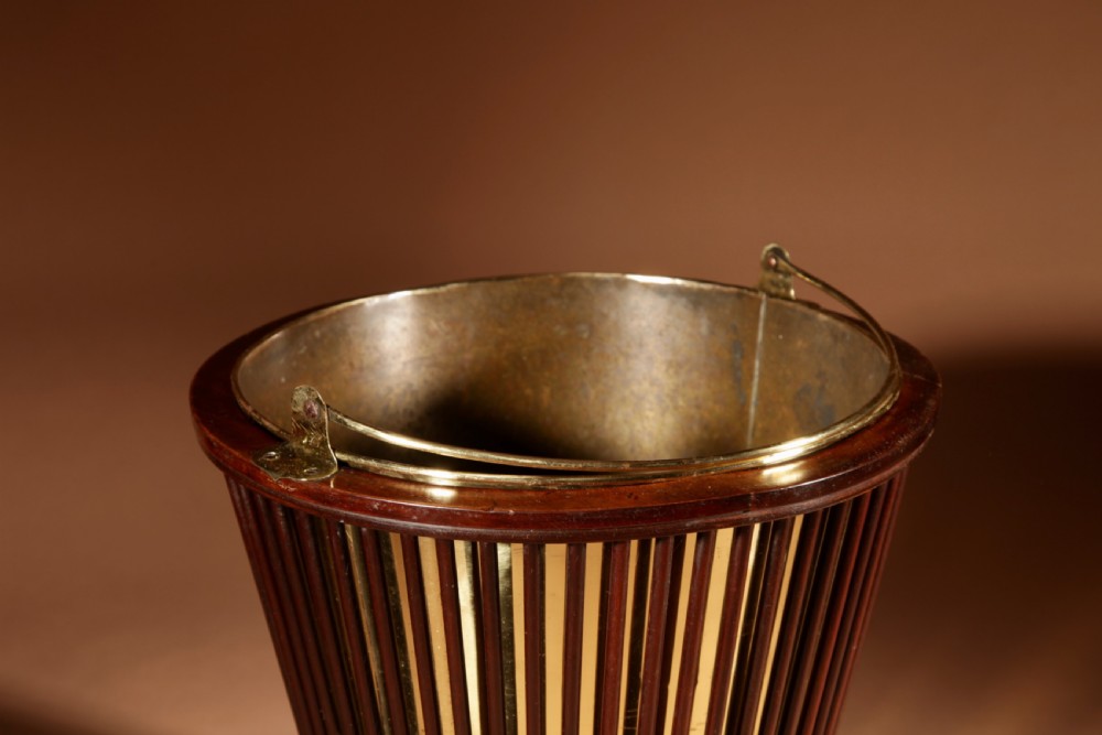 A 19th-century mahogany peat bucket constructed with open vertical spindles, a fitted brass interior liner, and a swinging brass handle. View VI