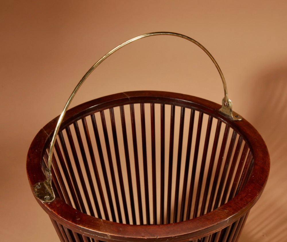 A 19th-century mahogany peat bucket constructed with open vertical spindles, a fitted brass interior liner, and a swinging brass handle. View X