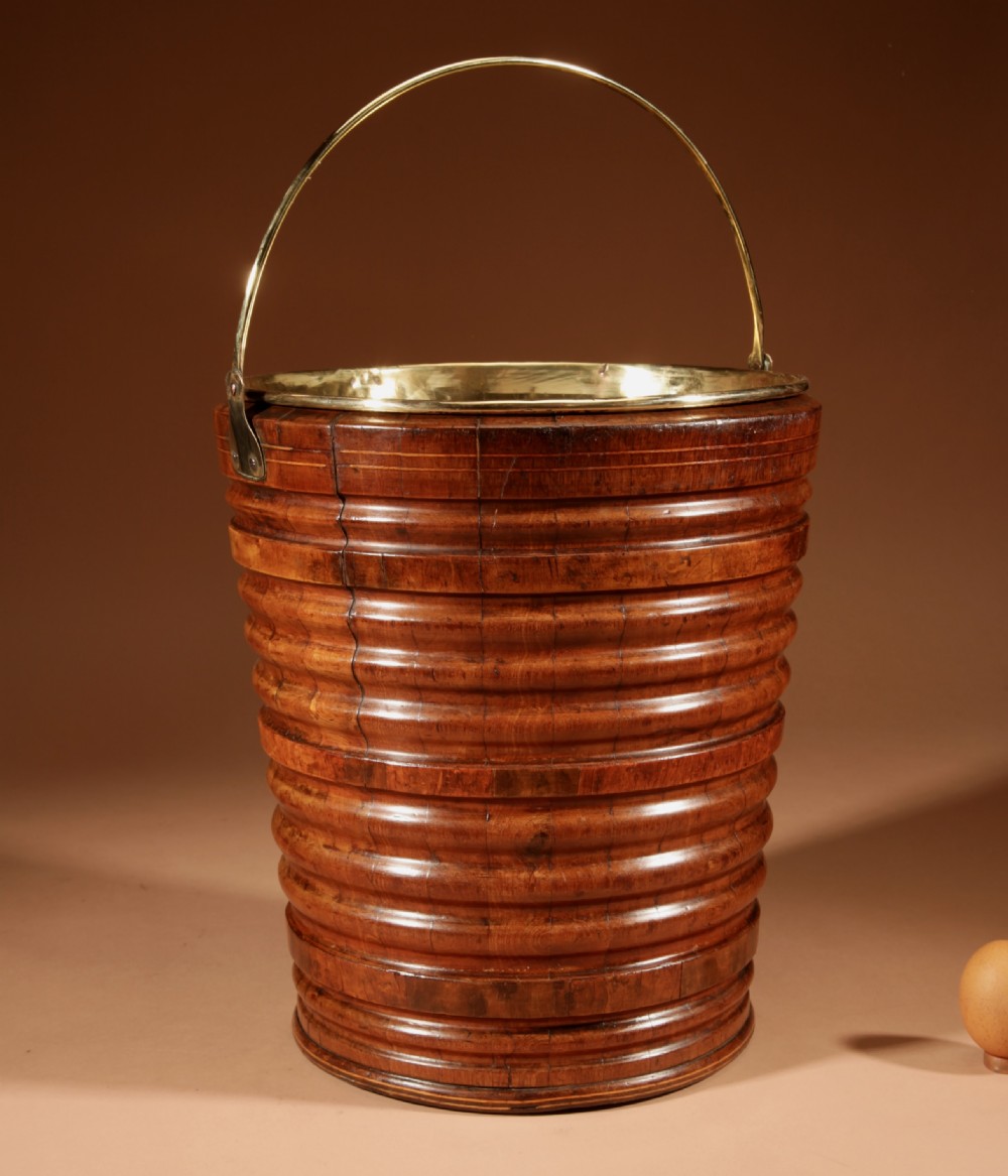 A tapered, coopered walnut bucket featuring horizontal ribbed bands, a fitted brass liner, and a brass swing handle. View V