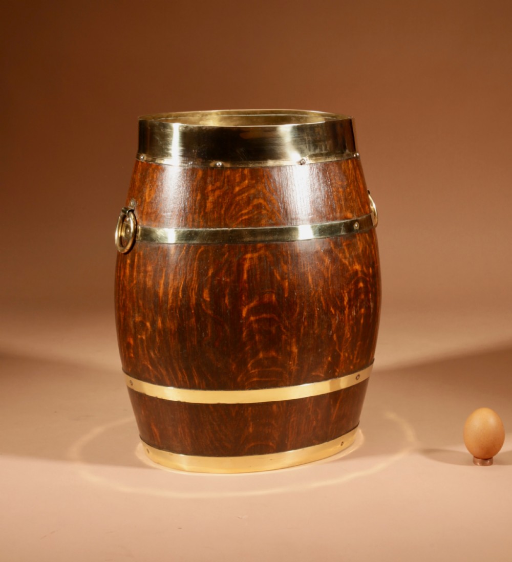 An oval coopered oak umbrella stand featuring polished brass binding straps and ring handles on the sides.