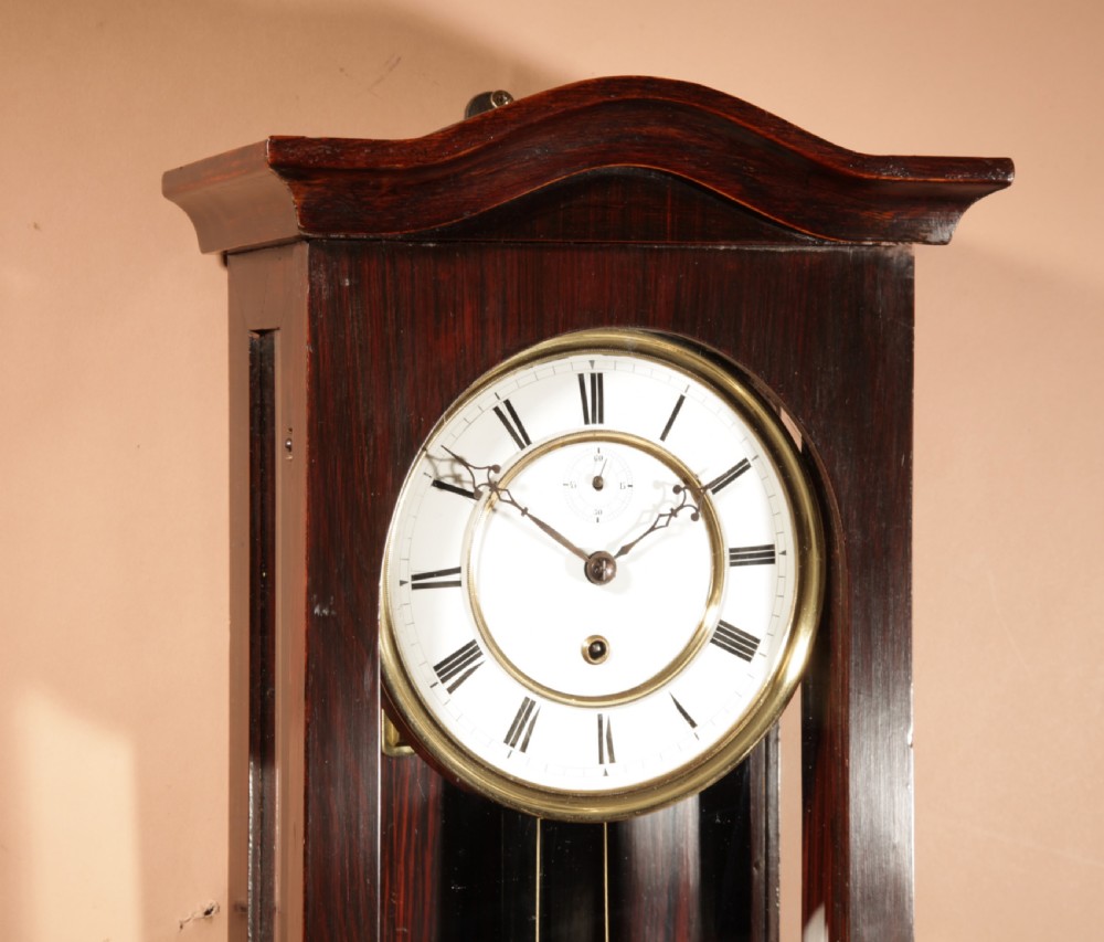 A nineteenth-century Black Forest wall clock in the Vienna regulator style, featuring a dark rosewood case, white enamel dial, and brass pendulum. View VII