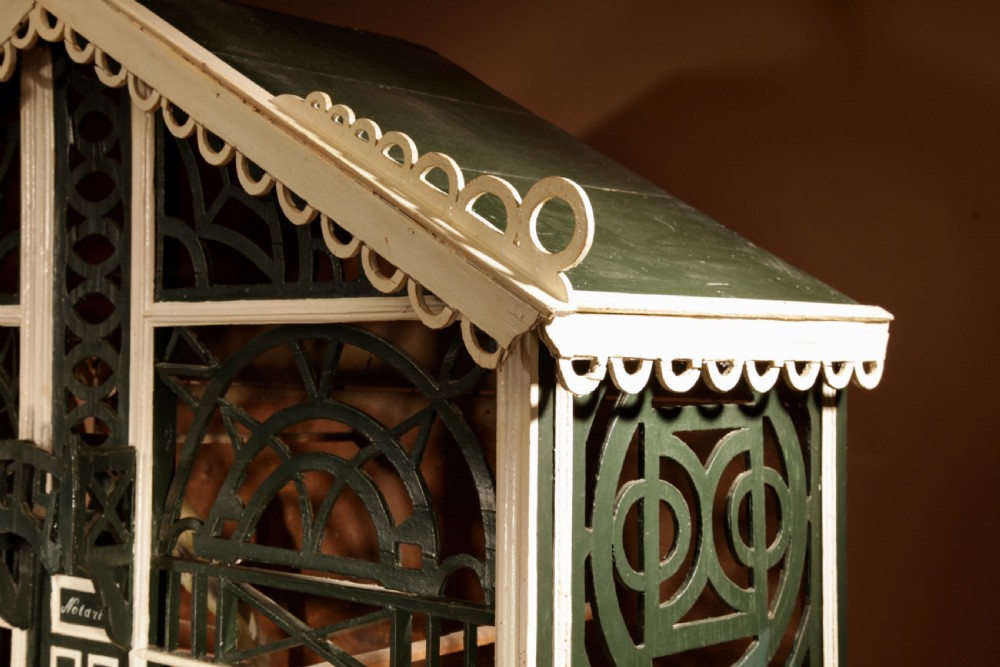 An Edwardian architectural wooden birdcage featuring dark green fretwork panels, cream trim, a gabled roof, and a miniature balcony stamped with the year 1914. View VIII