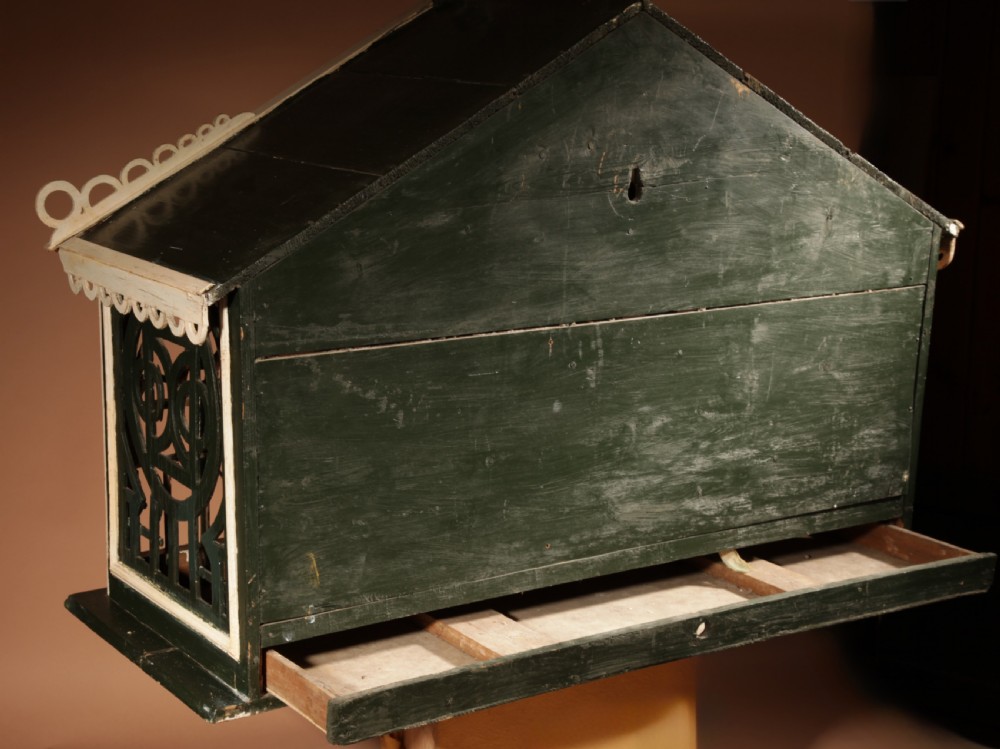 An Edwardian architectural wooden birdcage featuring dark green fretwork panels, cream trim, a gabled roof, and a miniature balcony stamped with the year 1914. View XI