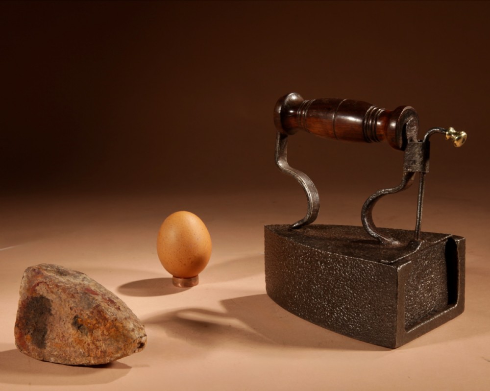 A Victorian cast iron box iron with a turned wooden handle, brass latch, and an accompanying iron slug on a plain background.