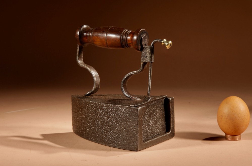 A Victorian cast iron box iron with a turned wooden handle, brass latch, and an accompanying iron slug on a plain background. View II
