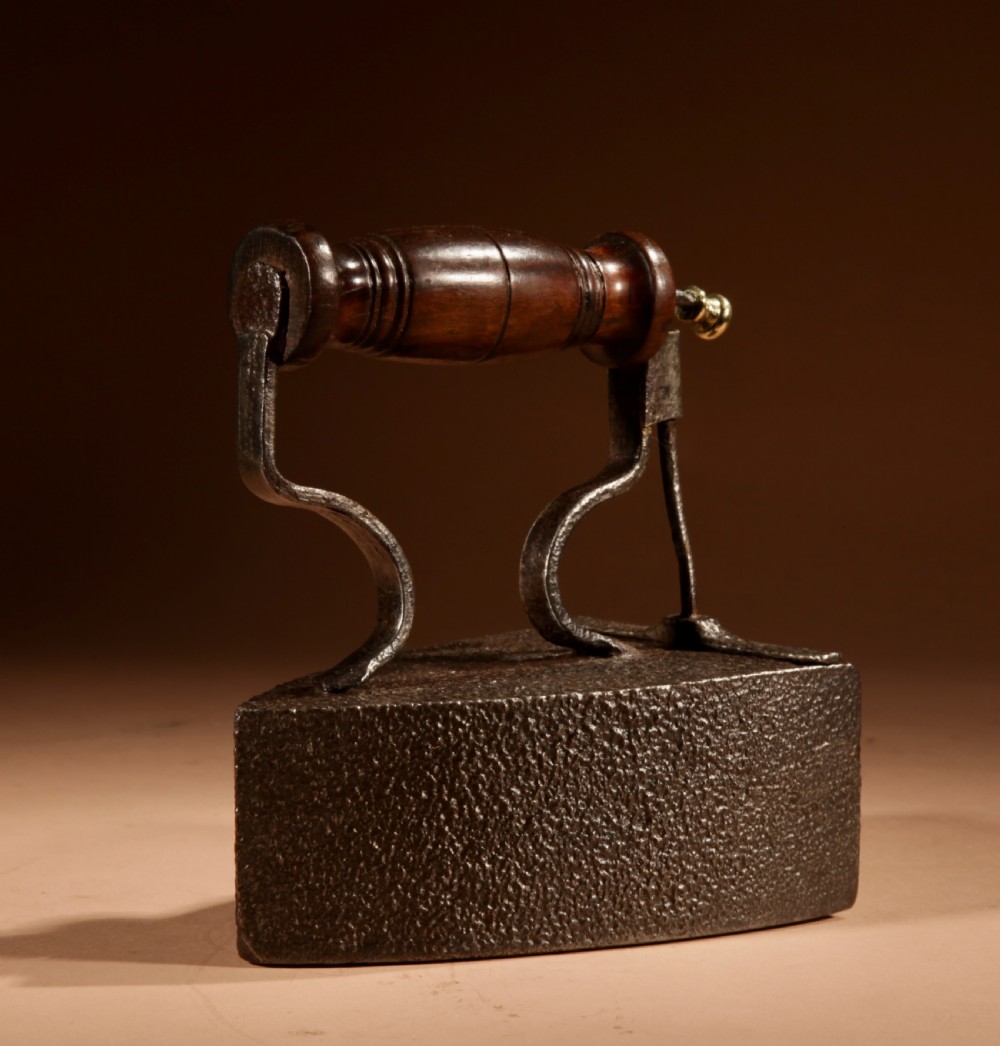 A Victorian cast iron box iron with a turned wooden handle, brass latch, and an accompanying iron slug on a plain background. View III