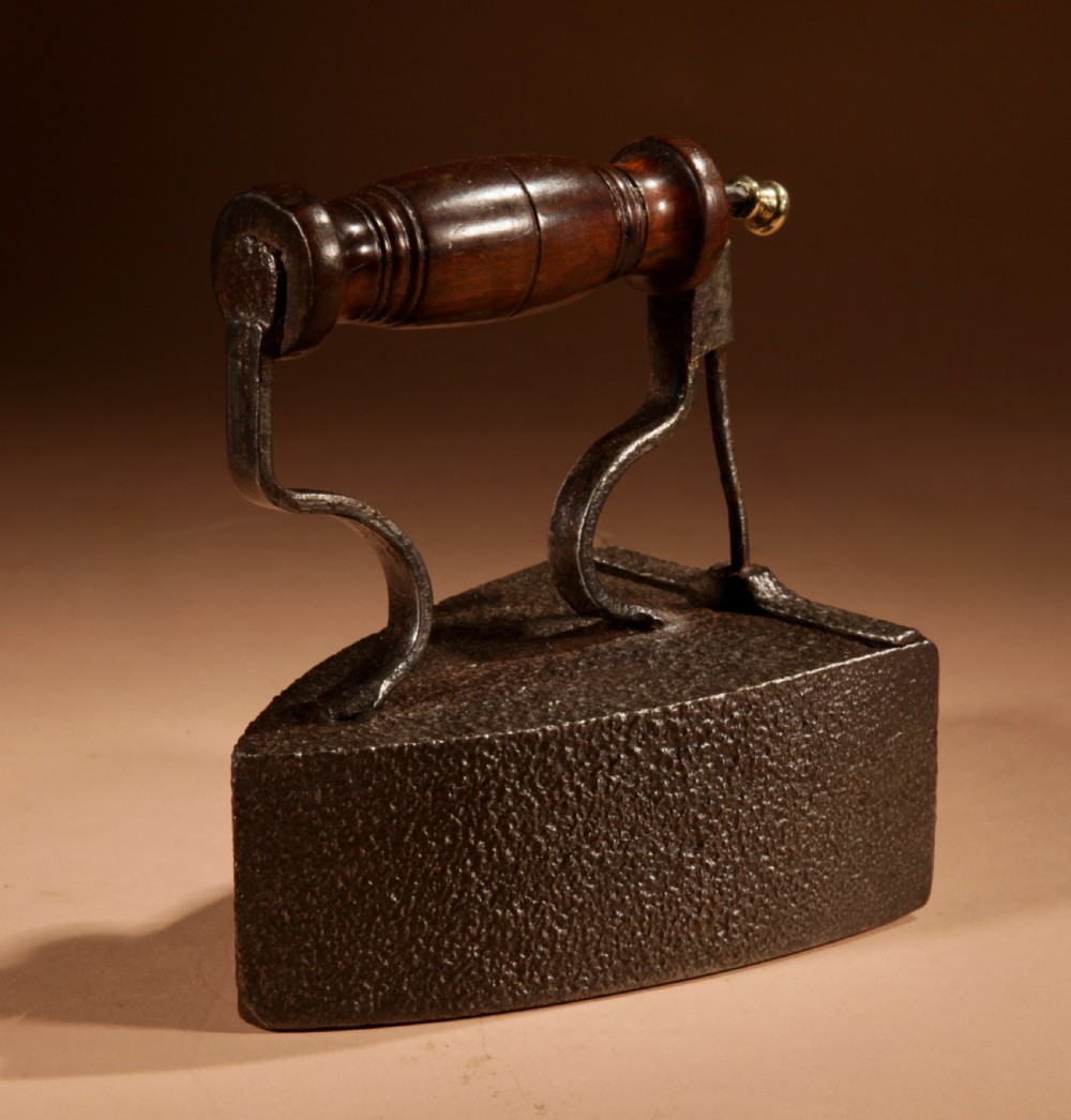 A Victorian cast iron box iron with a turned wooden handle, brass latch, and an accompanying iron slug on a plain background. View IV