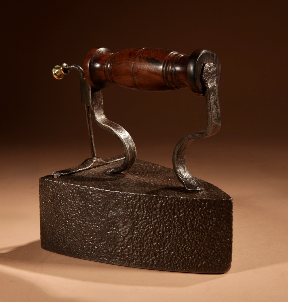 A Victorian cast iron box iron with a turned wooden handle, brass latch, and an accompanying iron slug on a plain background. View VII