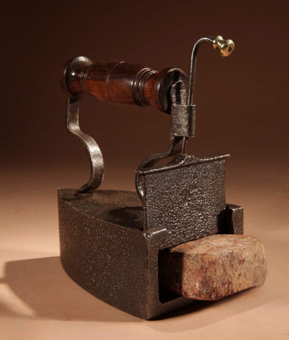 A Victorian cast iron box iron with a turned wooden handle, brass latch, and an accompanying iron slug on a plain background. View IX