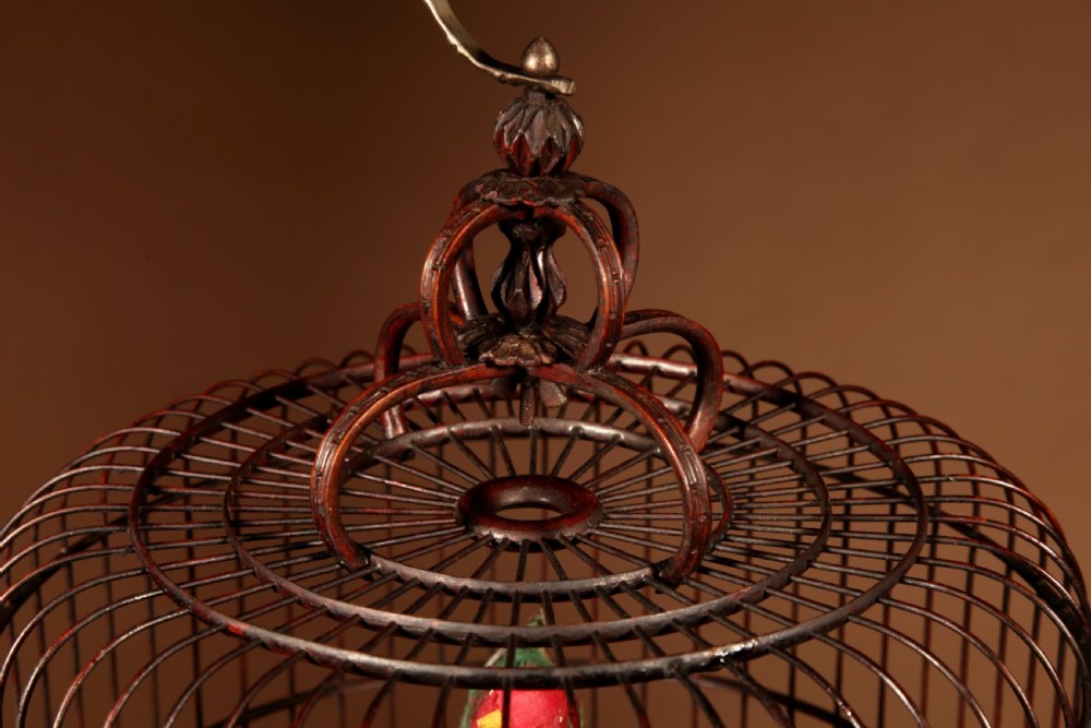 A cylindrical dark brown bamboo birdcage featuring a metal hanging hook, carved base trim, internal perch, and miniature blue and white porcelain cups. View IX