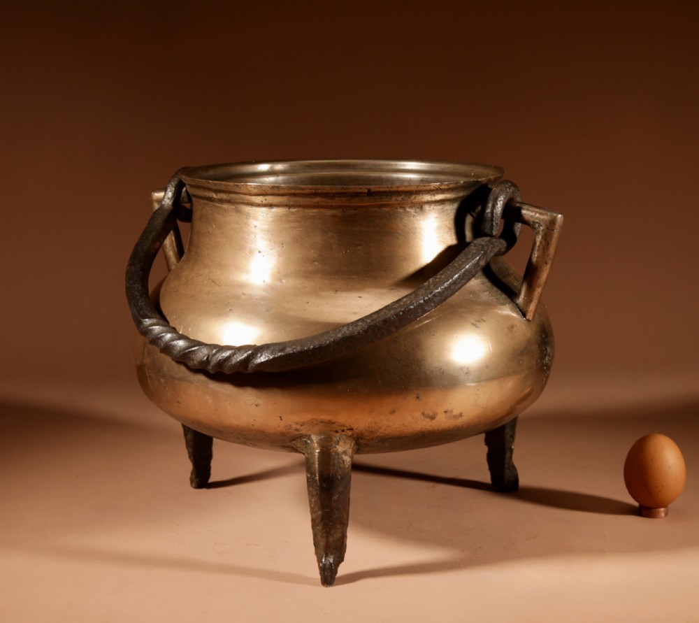 A 17th-century Continental bronze tripod cauldron featuring a bulbous body, three pointed feet, side handles, and a twisted wrought iron swing handle.