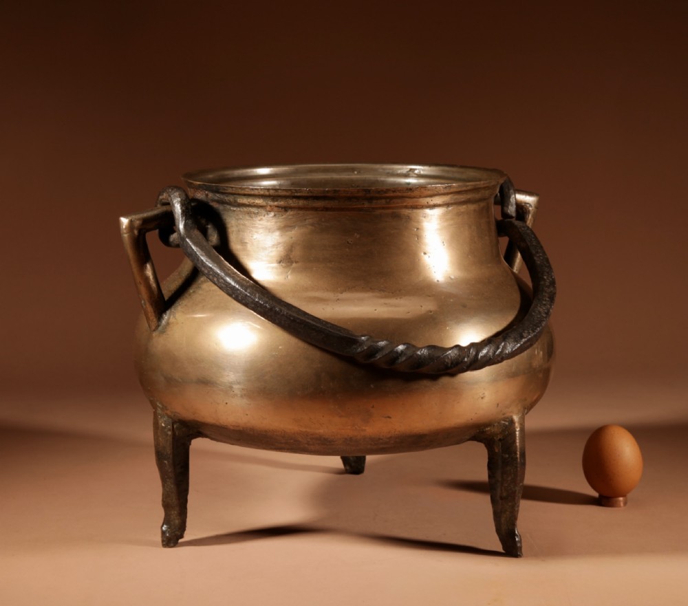 A 17th-century Continental bronze tripod cauldron featuring a bulbous body, three pointed feet, side handles, and a twisted wrought iron swing handle. View II