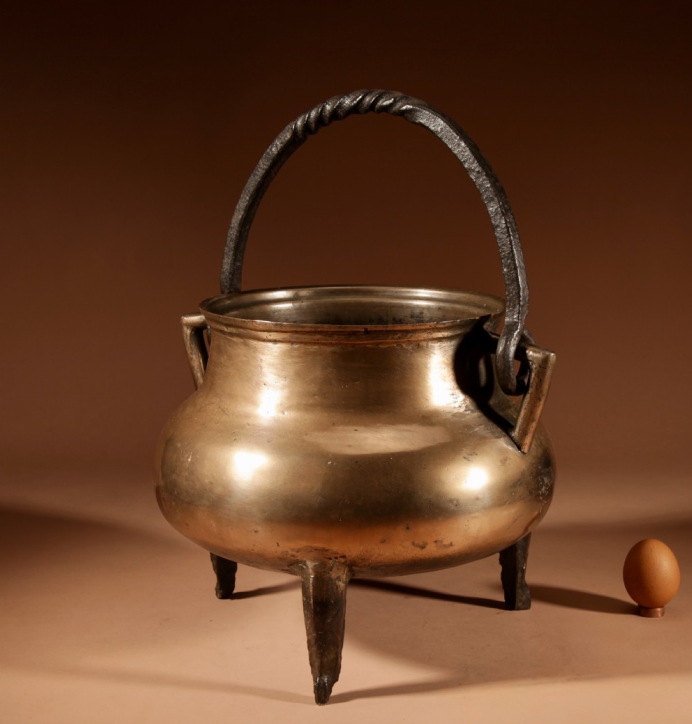A 17th-century Continental bronze tripod cauldron featuring a bulbous body, three pointed feet, side handles, and a twisted wrought iron swing handle. View IV