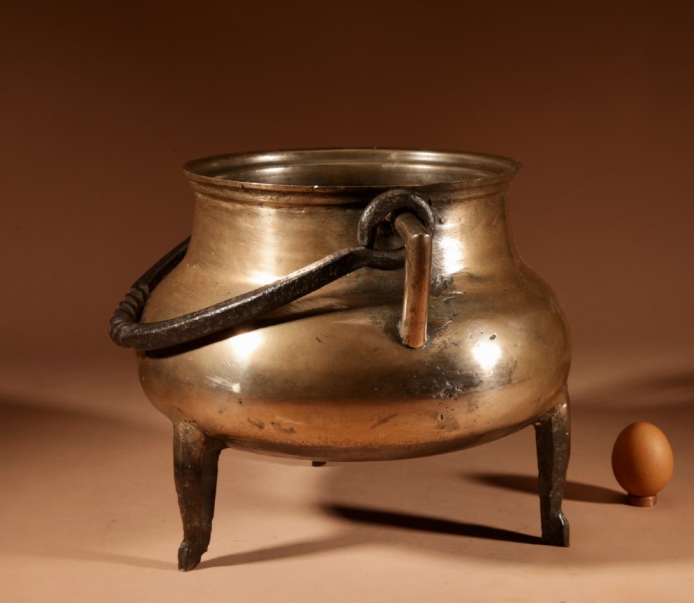 A 17th-century Continental bronze tripod cauldron featuring a bulbous body, three pointed feet, side handles, and a twisted wrought iron swing handle. View V