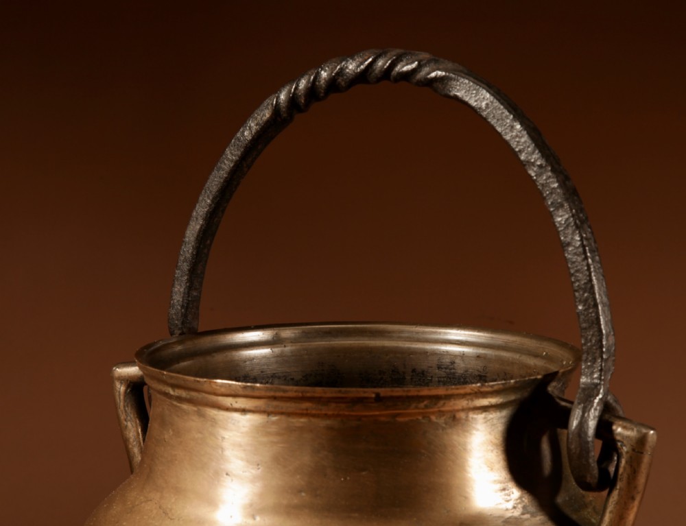 A 17th-century Continental bronze tripod cauldron featuring a bulbous body, three pointed feet, side handles, and a twisted wrought iron swing handle. View VI