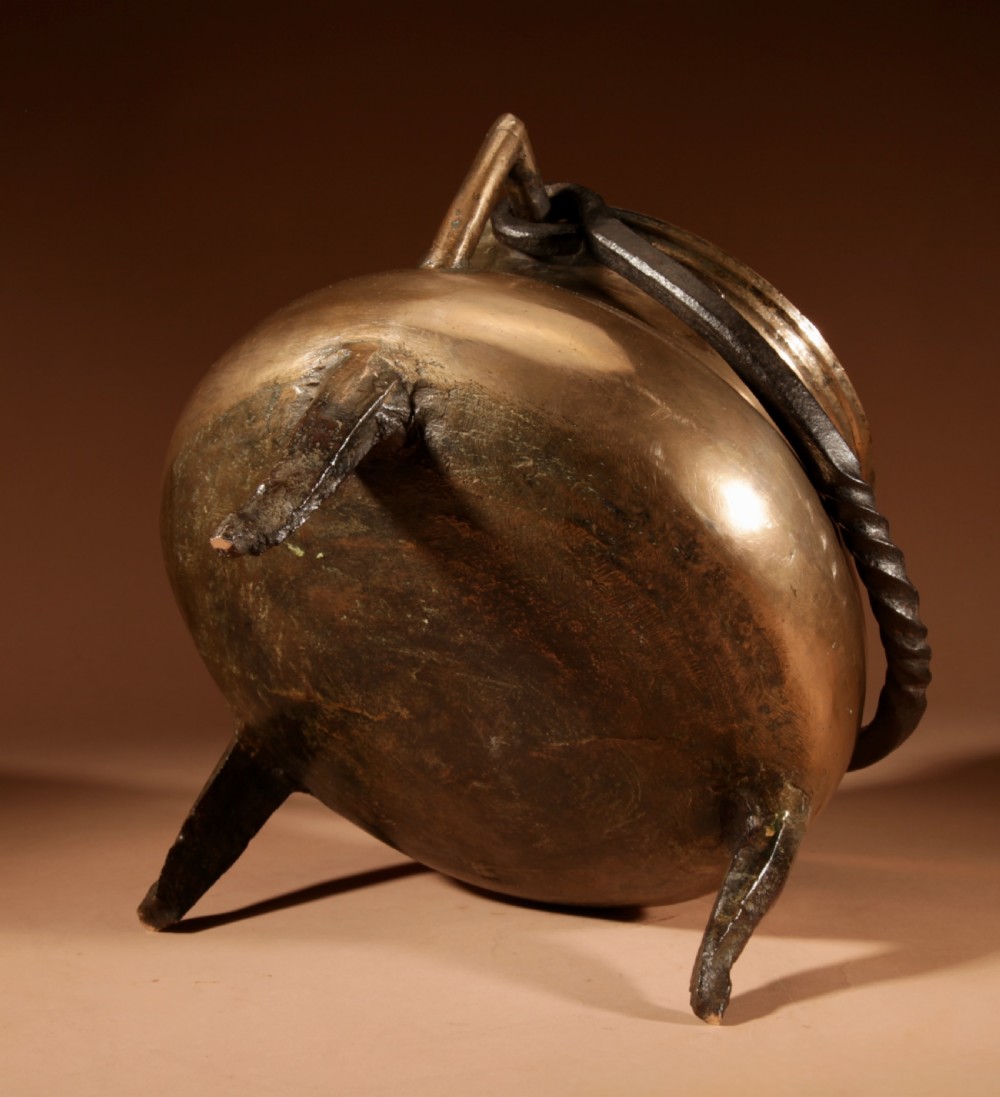 A 17th-century Continental bronze tripod cauldron featuring a bulbous body, three pointed feet, side handles, and a twisted wrought iron swing handle. View X