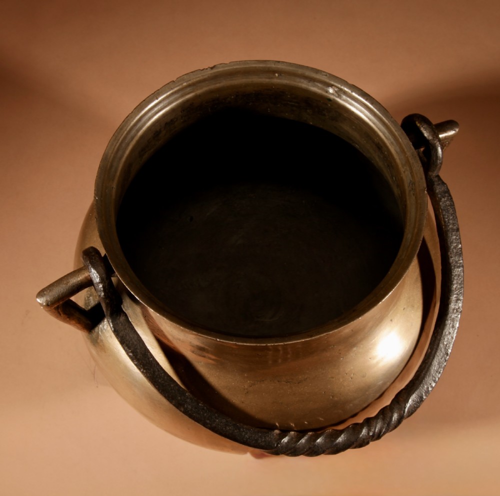 A 17th-century Continental bronze tripod cauldron featuring a bulbous body, three pointed feet, side handles, and a twisted wrought iron swing handle. View XI