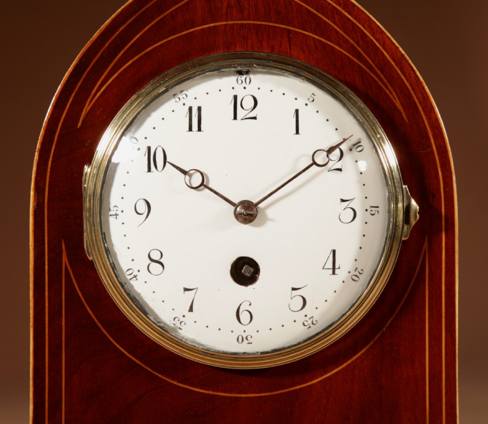 An Edwardian inlaid mahogany mantel clock with a lancet arch top, white enamel dial with Arabic numerals, and brass bun feet. View II
